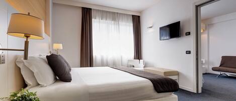 A hotel room with a bed, bedside lamps, a TV, a desk, and a chair.