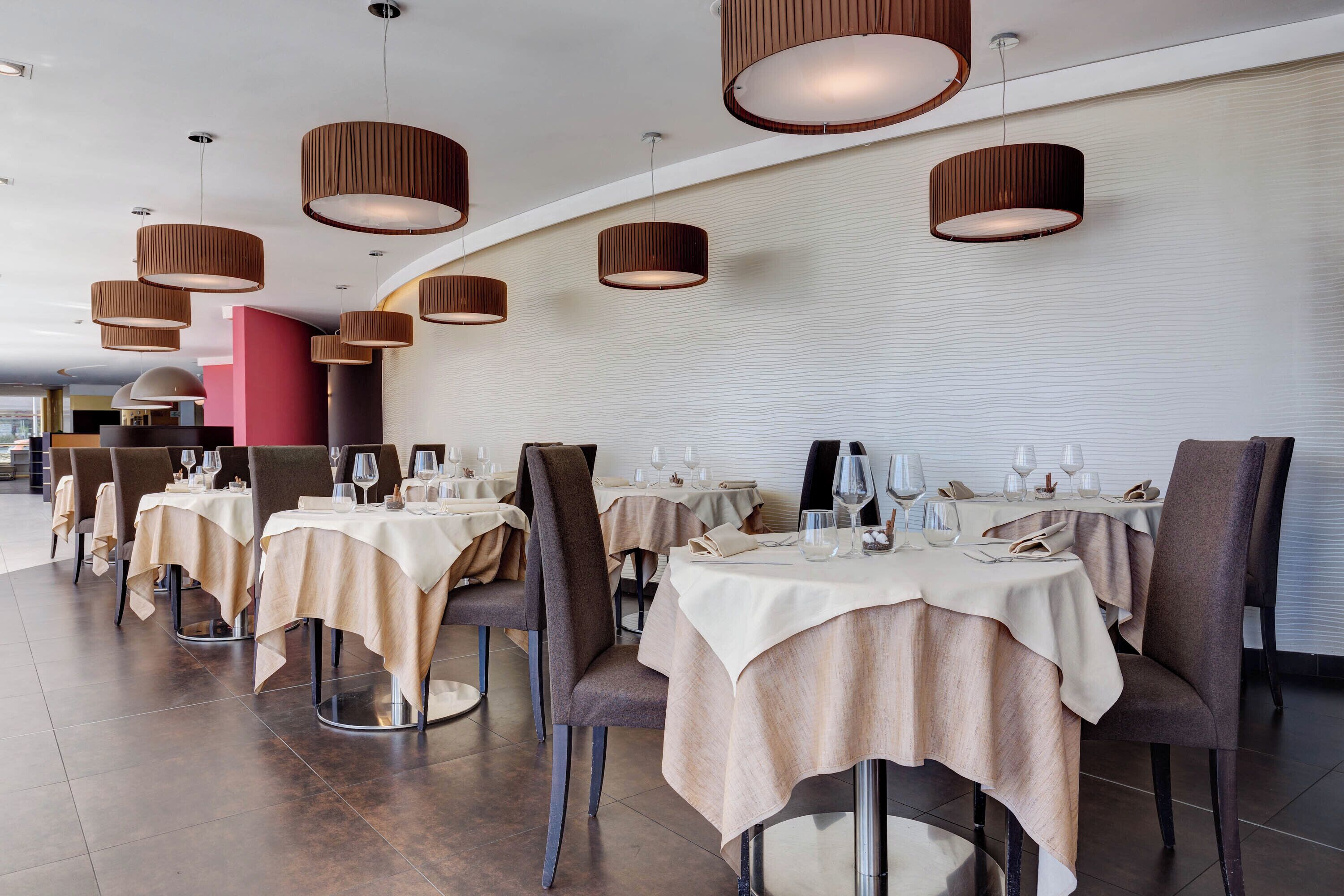 Un restaurante moderno con mesas redondas, lámparas colgantes marrones y un diseño limpio y minimalista.