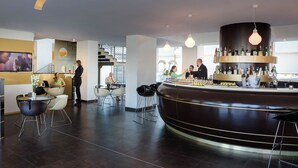 A modern bar area with a curved counter, bar stools, and a variety of bottles and glasses. - iH Hotels Roma Z3 (Rome)