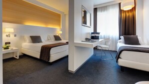 A hotel room with two beds, a desk, a chair, and a large window with curtains. - iH Hotels Roma Z3 (Rome)