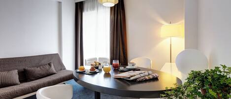 A modern hotel room with a round dining table, a sofa, and a potted plant.