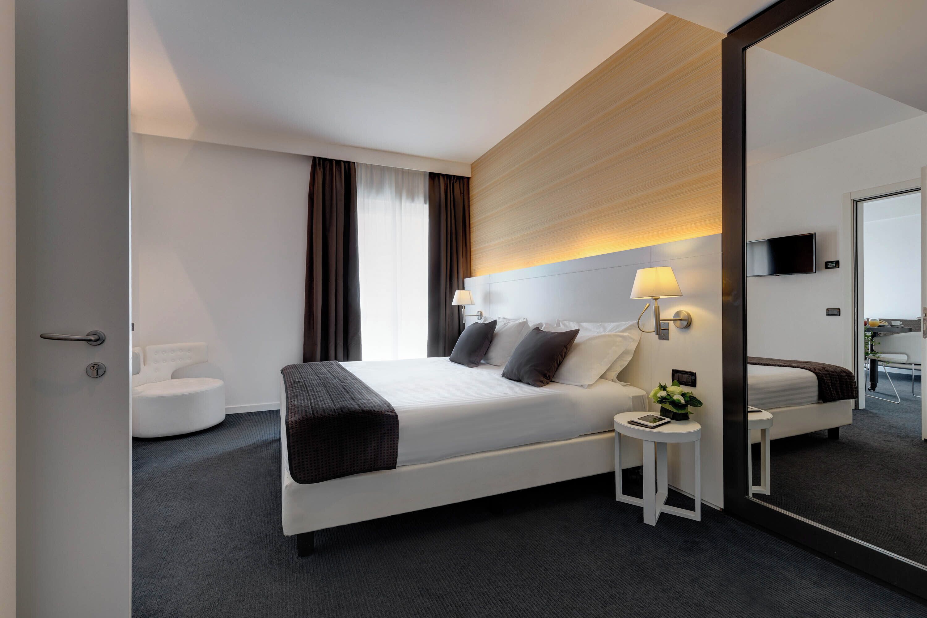 A modern hotel room with a large bed, bedside tables, a mirror, and a television.