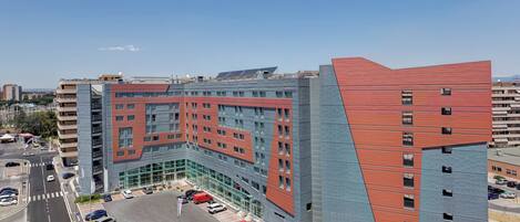 A modern building with a unique angular design, featuring multiple floors and a parking area with several cars.