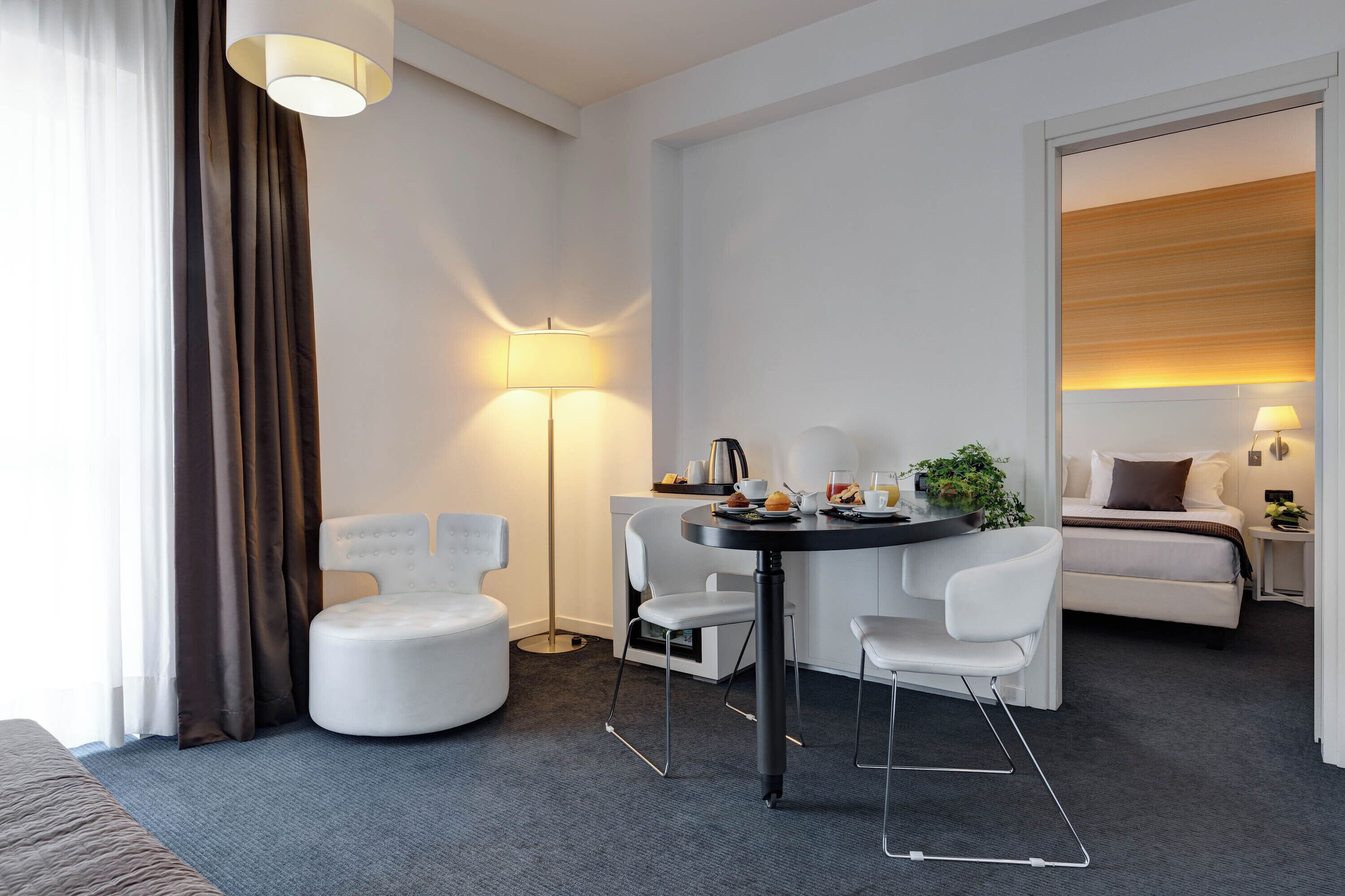 A modern hotel room with a dining area, a bed, and a large window with curtains.