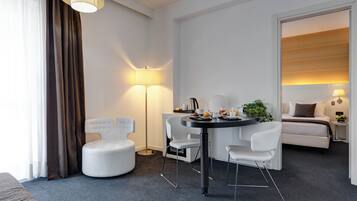 Een moderne hotelkamer met een zithoek, een bed en een groot raam met gordijnen.