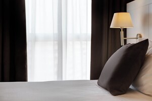 Habitación de hotel con cama, lámpara y ventana con cortinas.
