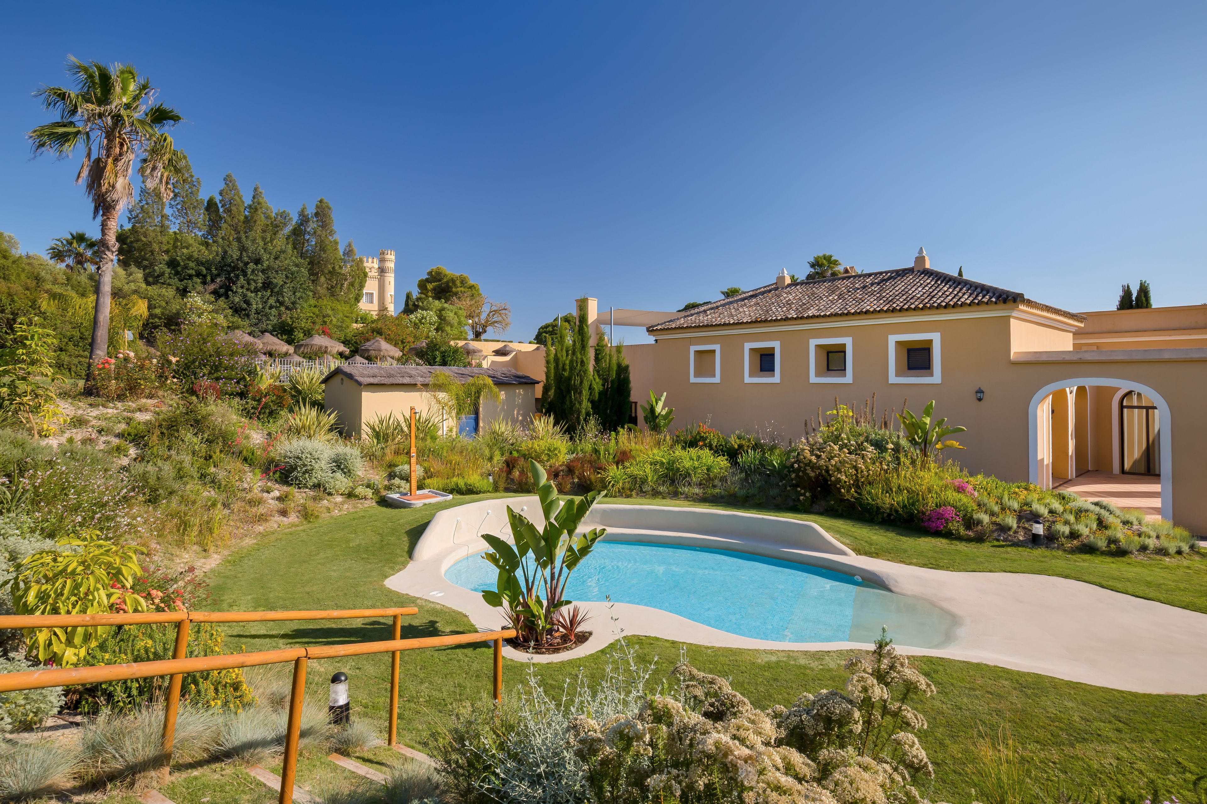 Un giardino curato con piscina, una grande casa con torre e un cielo azzurro limpido.