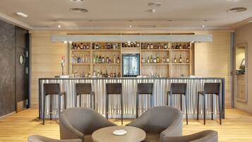 A bar area with a wooden counter, multiple shelves of bottles, and bar stools.