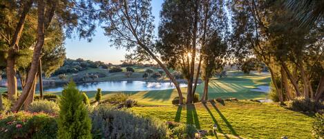A golf course with a pond, surrounded by trees and well-maintained grass.