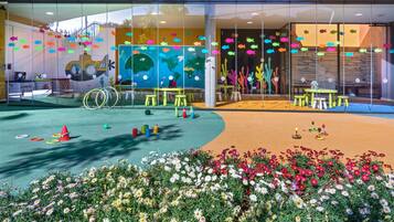 A colorful indoor play area with a globe mural, play tables, and a flower garden.