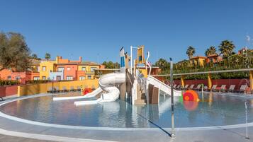 A swimming pool with a water slide, lounge chairs, and a view of colorful buildings in the background.