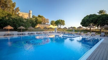 Relax by the serene pool surrounded by lush greenery and a historic castle.