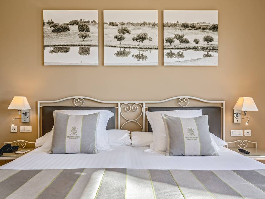 A hotel room with a large bed, two bedside tables, a nightstand, and three landscape paintings on the wall.