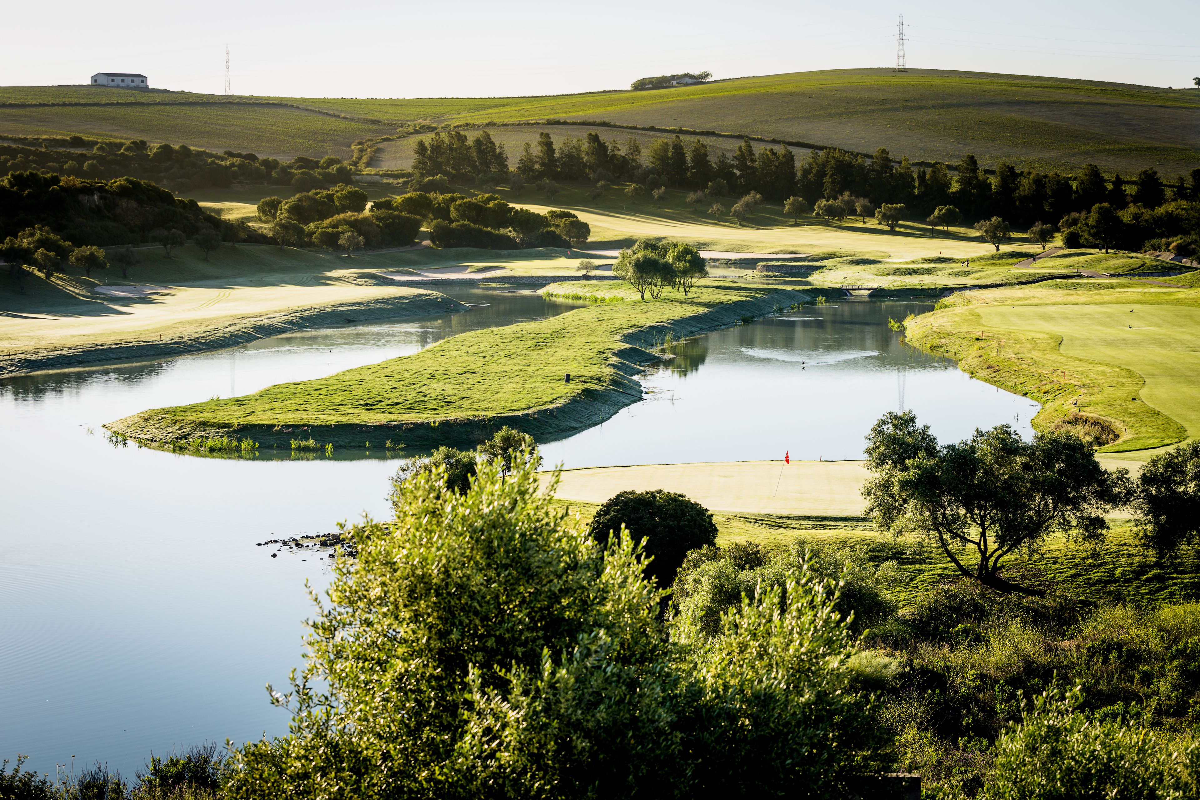 A golf course with a pond, trees, and a distant building.