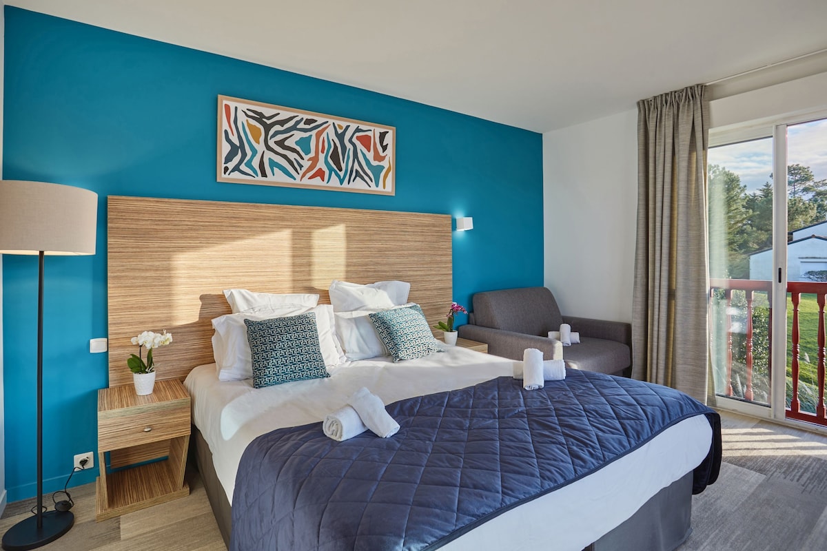 Une chambre d’hôtel avec un grand lit, une tête de lit en bois, un mur d’accent bleu, une lampe sur pied et une vue sur l’extérieur.