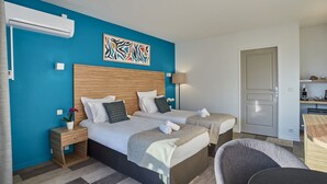 Hotellihuone, jossa on kaksi sänkyä, sininen tehosteseinä, puinen sängynpääty, työpöytä ja tuoli.