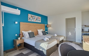 A hotel room with two beds, a blue accent wall, a modern lamp, and a door leading to the bathroom.