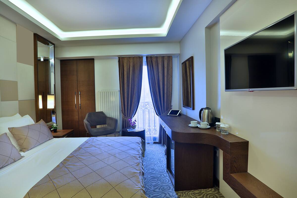 A hotel room with a bed, a desk, a chair, a TV, and a window with curtains.