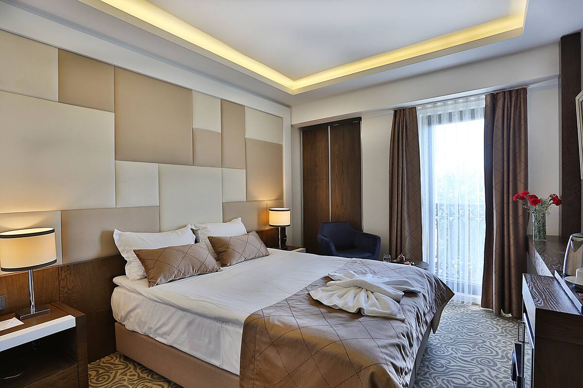 A hotel room with a large bed, a desk, a chair, and a window with curtains.
