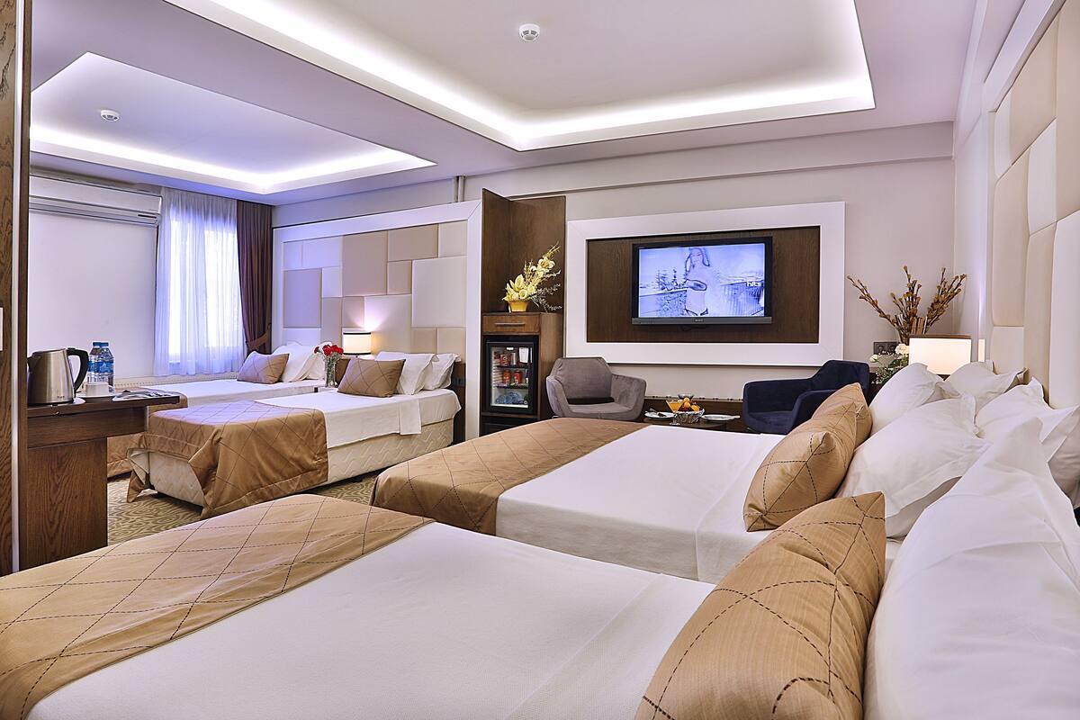 A hotel room with two beds, a TV, a desk with a lamp, and a minibar.