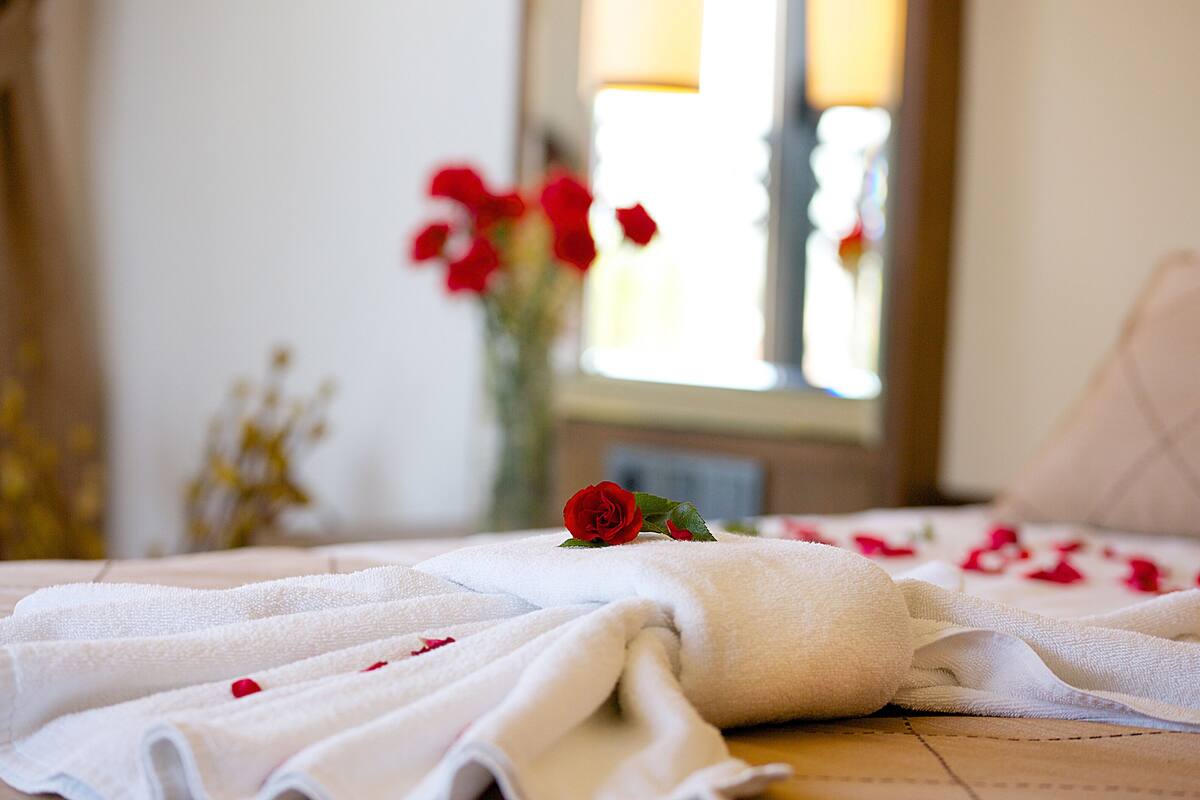 A neatly arranged bed with white towels and a single red rose, suggesting a clean and well-maintained room.