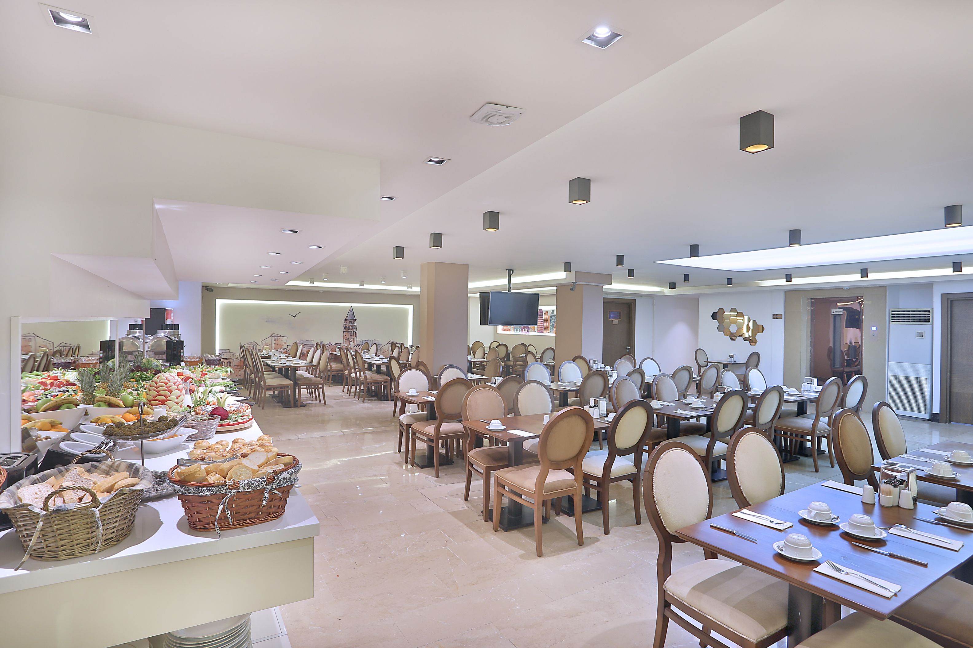 A spacious dining area with multiple tables and chairs, a buffet with various food items, and a modern ceiling design.