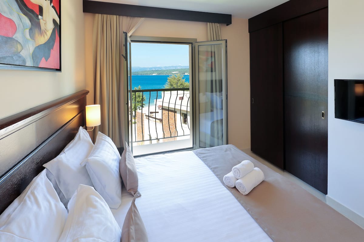 Habitación de hotel con una cama grande, televisión, balcón con vista al mar y un cuadro en la pared.