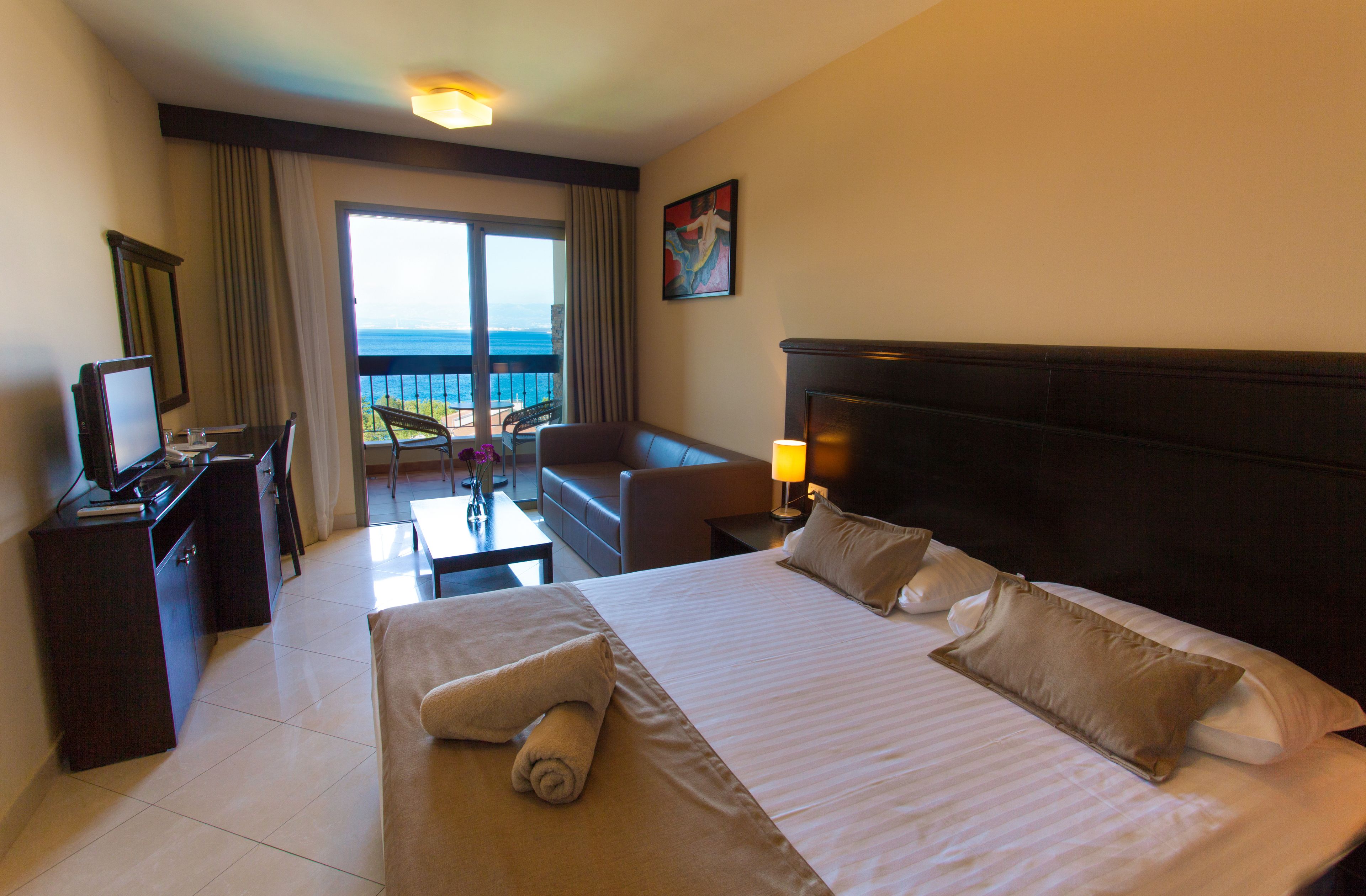 Una habitación de hotel con una cama, un escritorio, una silla, un sofá y vistas al océano a través de un ventanal grande.