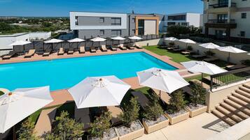 Un espace piscine moderne, doté de chaises longues et de parasols, entouré de bâtiments avec balcons et offrant une vue dégagée sur le paysage.