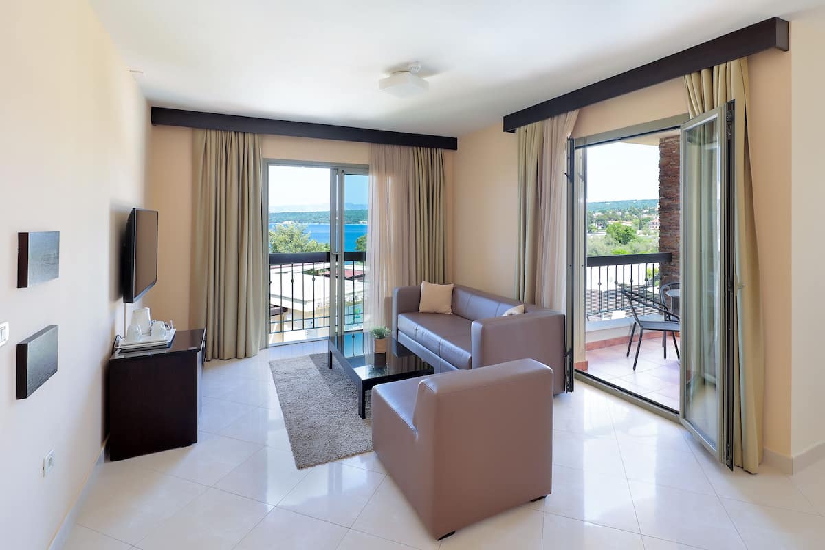 Una sala de estar moderna con un sofá, una mesa de centro y un televisor. Hay un balcón con vistas al mar.