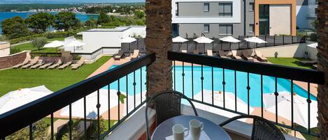 Ein Balkon mit Pool, Liegestühlen und Sonnenschirmen, mit Blick auf ein modernes Gebäude und die Küste.