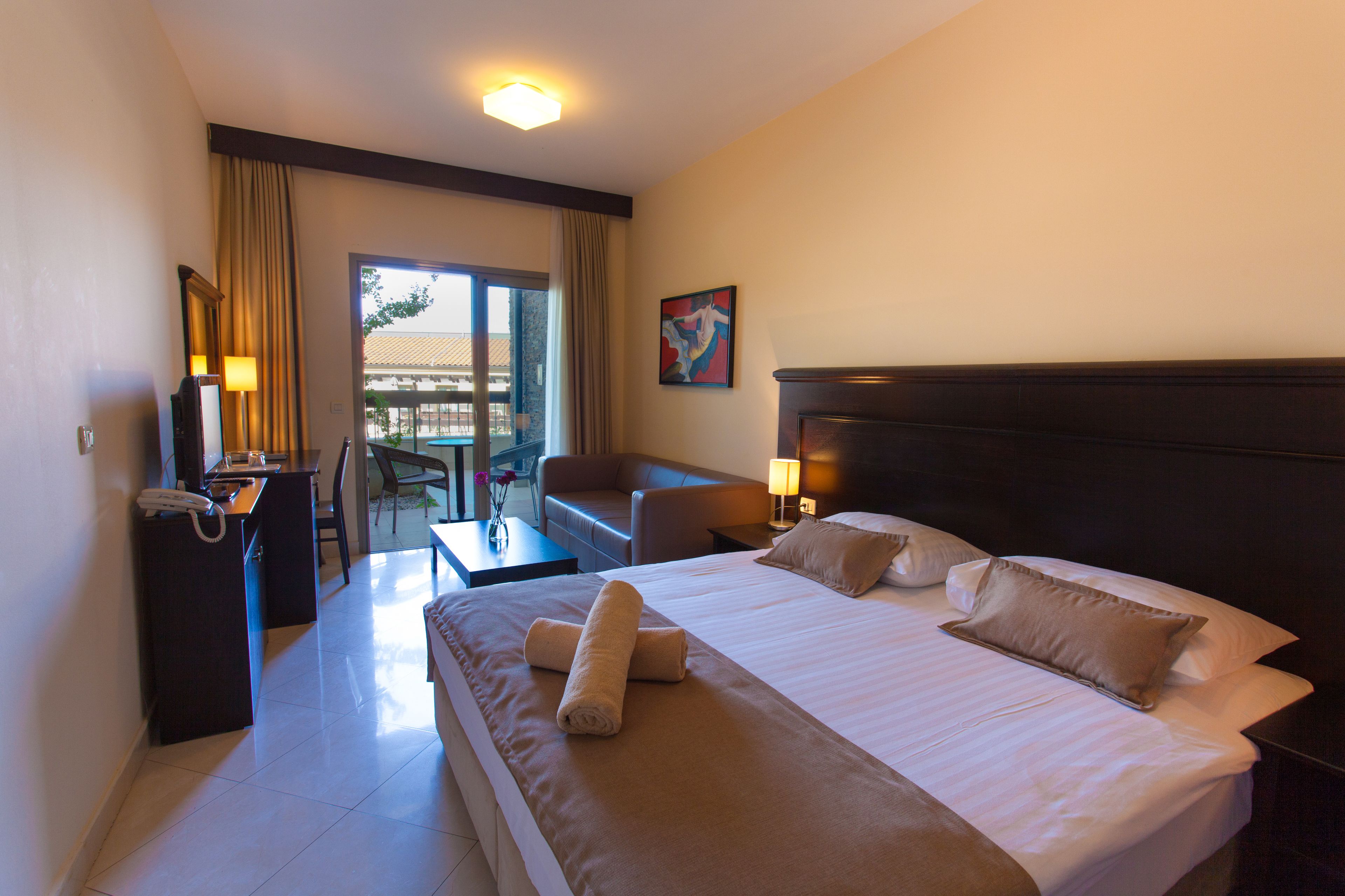 Habitación de hotel con una cama grande, un escritorio con teléfono, una silla y vistas al exterior a través de un ventanal.