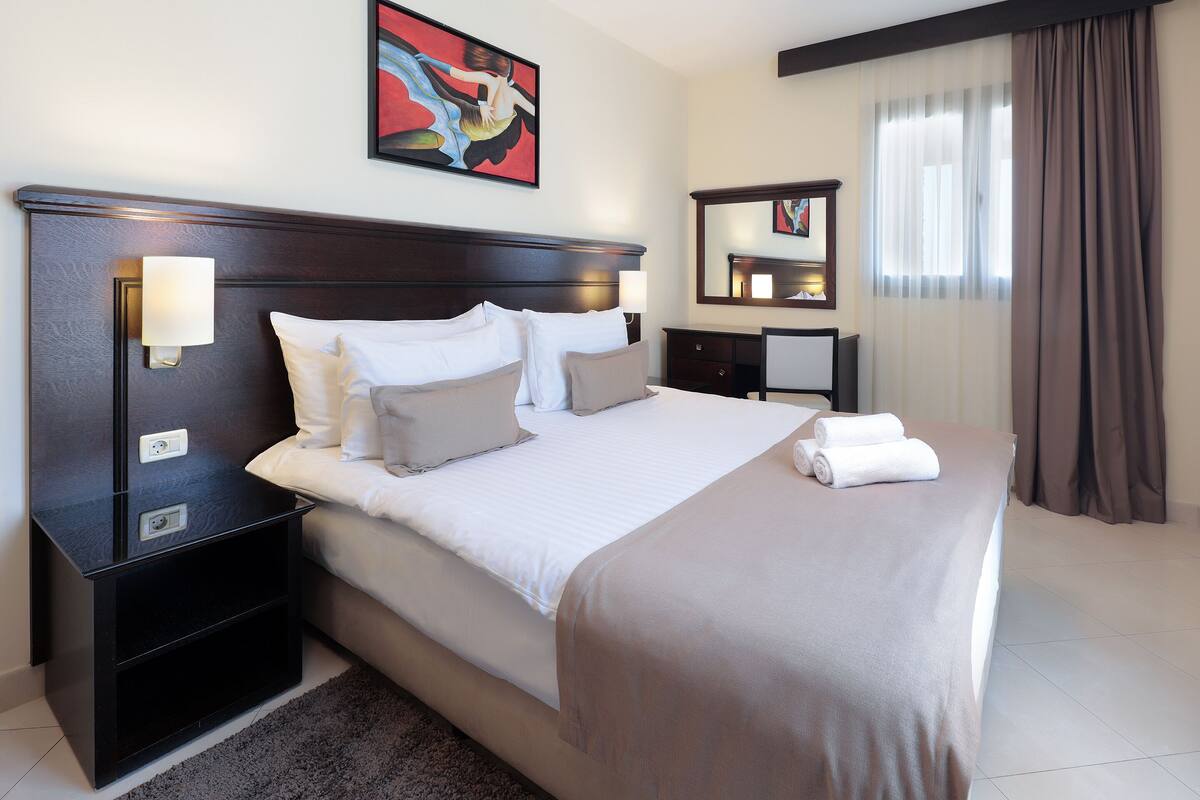 Una habitación de hotel con una cama grande, mesitas de noche, un escritorio y una silla.