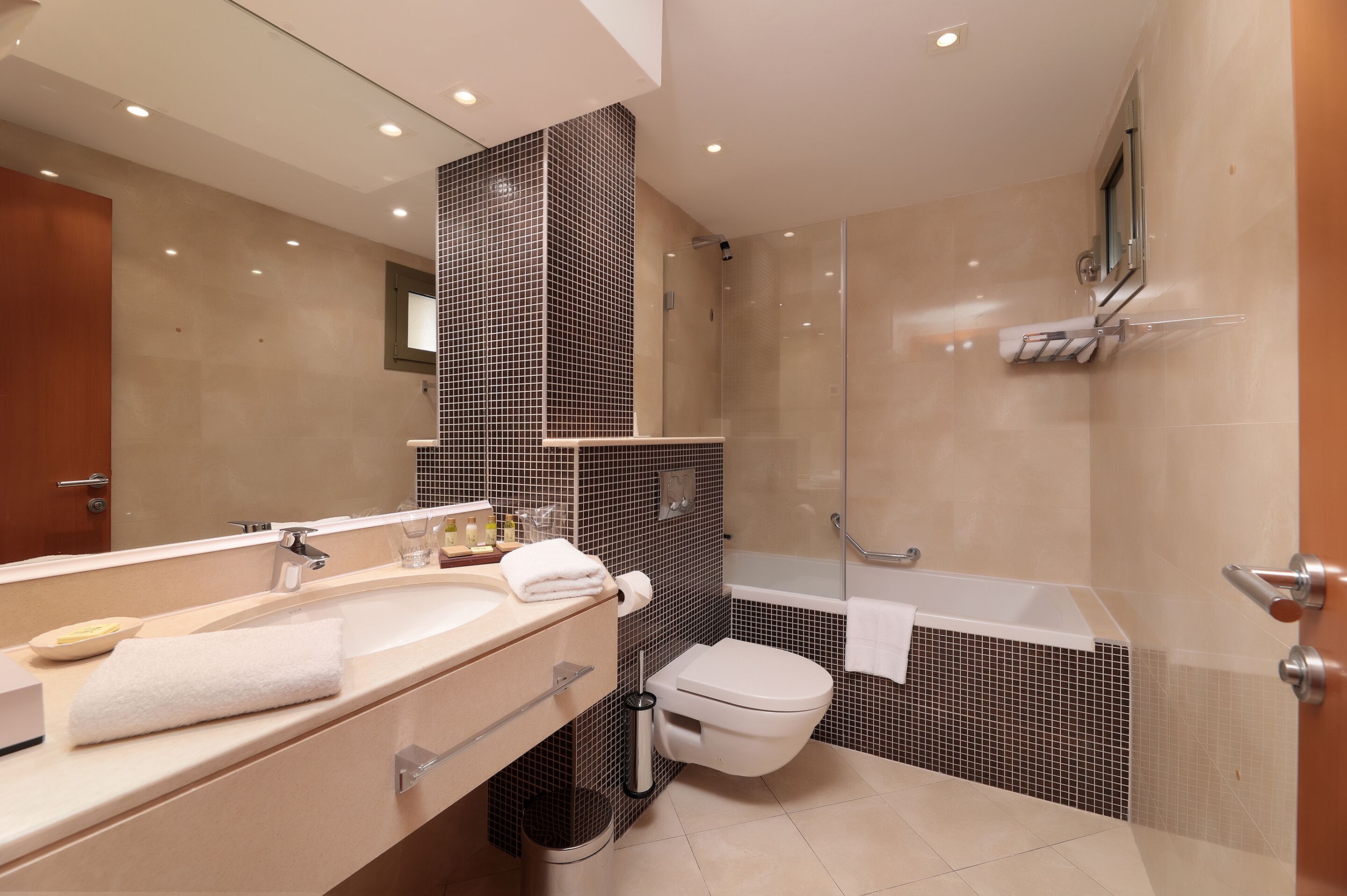 Un baño moderno con un espejo grande, un lavamanos, un inodoro y una zona de ducha.