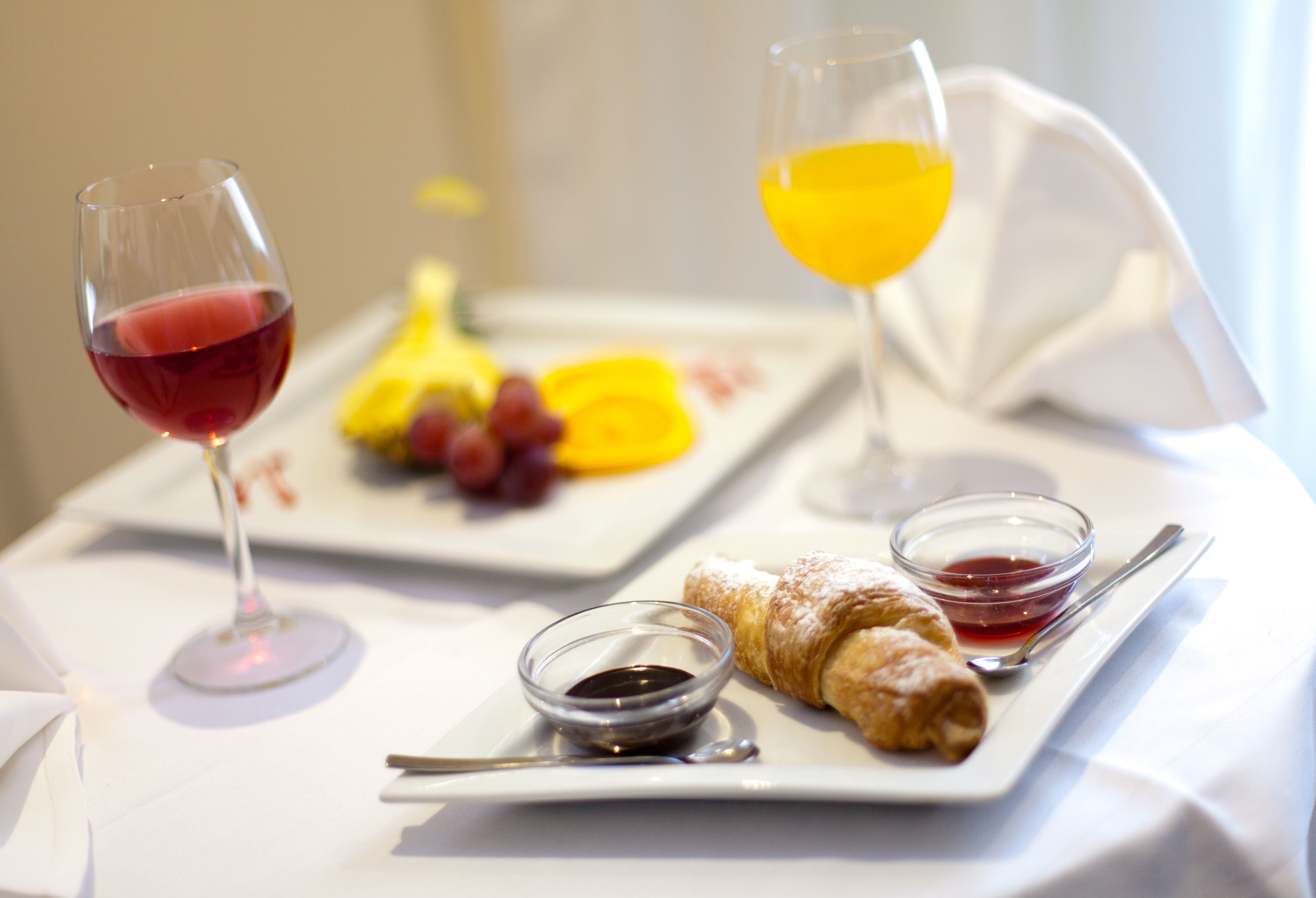 A breakfast setting with a croissant, fruit, and two glasses of beverage on a white tablecloth.