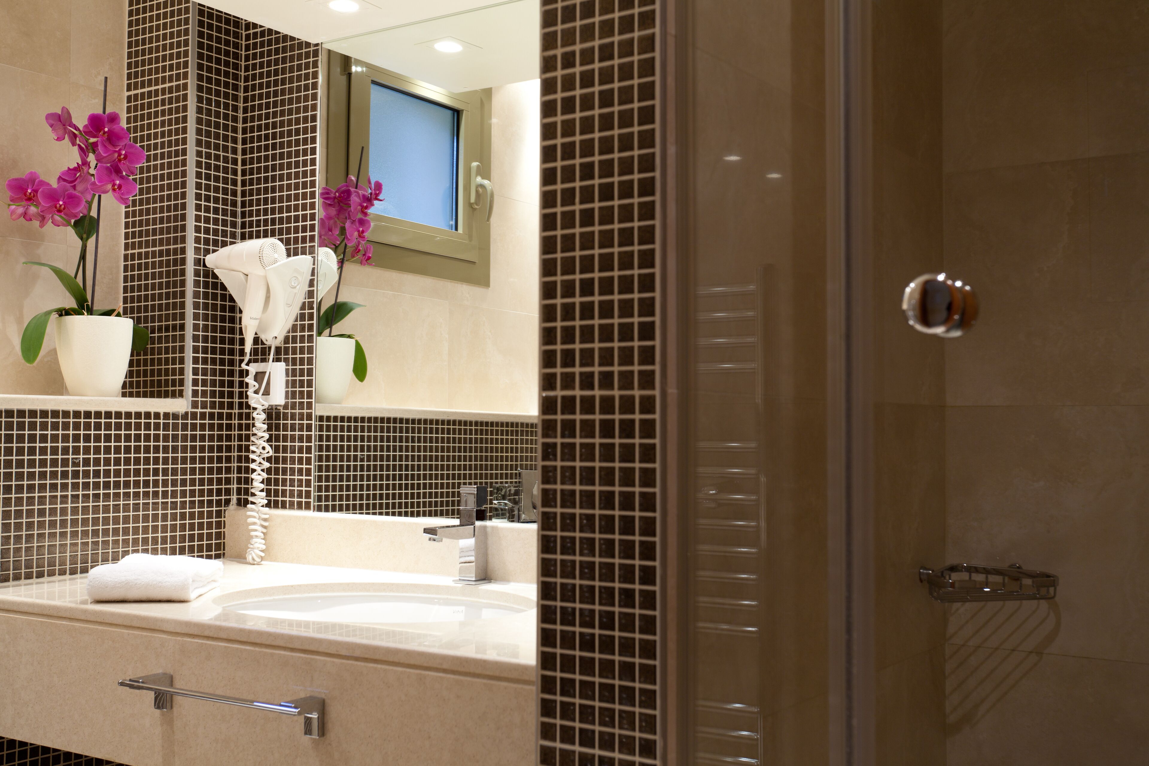 A bathroom with a sink, mirror, and potted orchids.