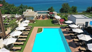A pool area with lounge chairs and umbrellas, a restaurant, and a view of the sea. - Blue Waves Resort (Malinska-Dubasnica)