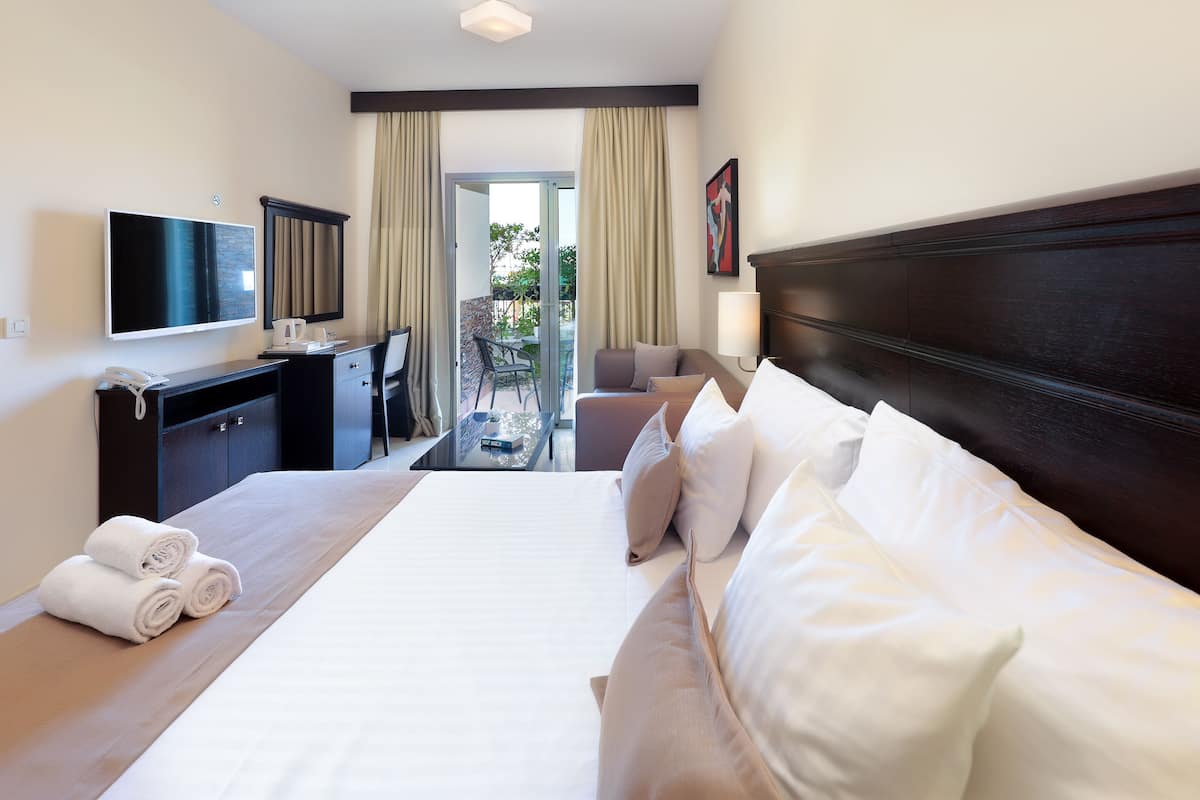 Habitación de hotel con una cama grande, un escritorio con televisor, una silla y vistas al exterior.