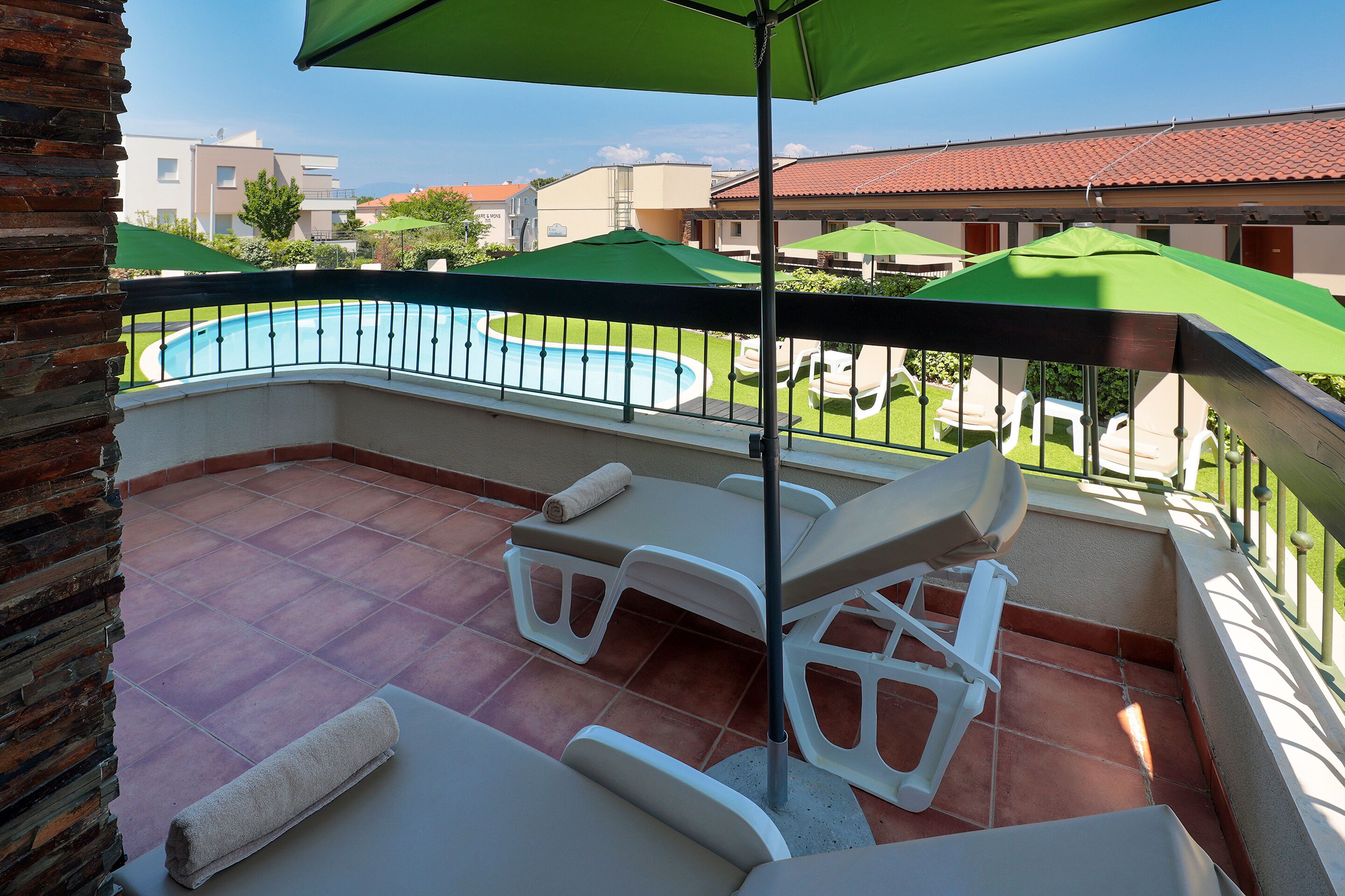Un balcone con piscina, poltrone da relax bianche e ombrelloni verdi.
