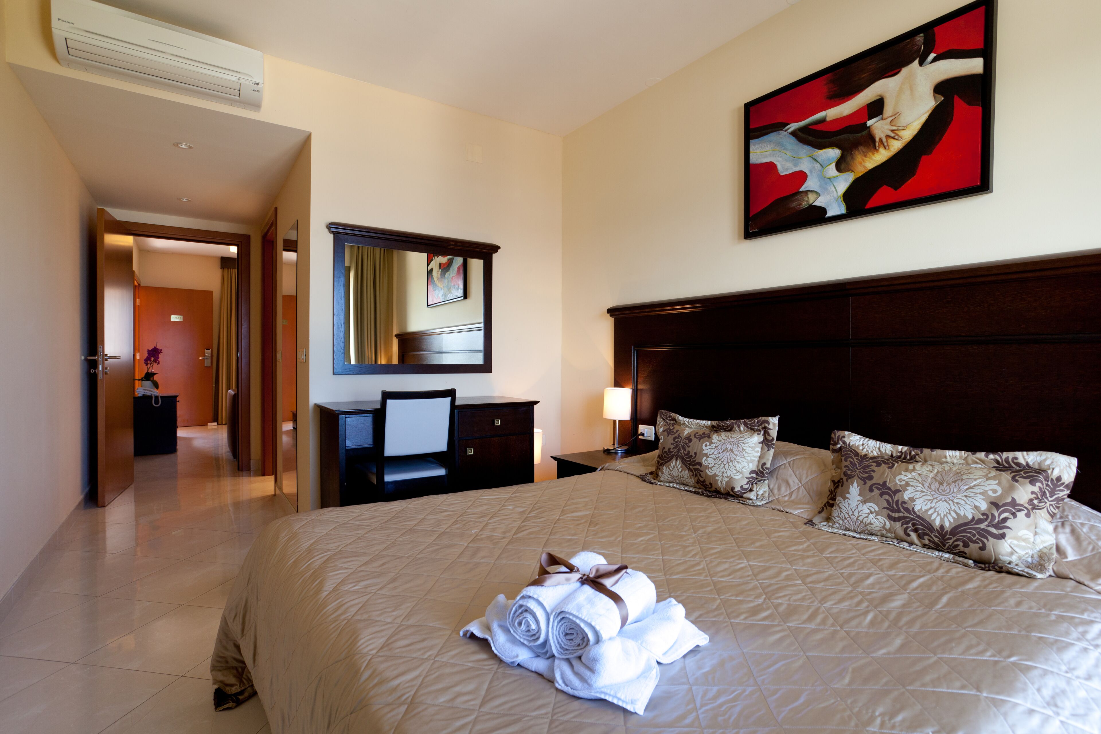 A hotel room with a large bed, a desk, a chair, a dresser, and a painting on the wall.