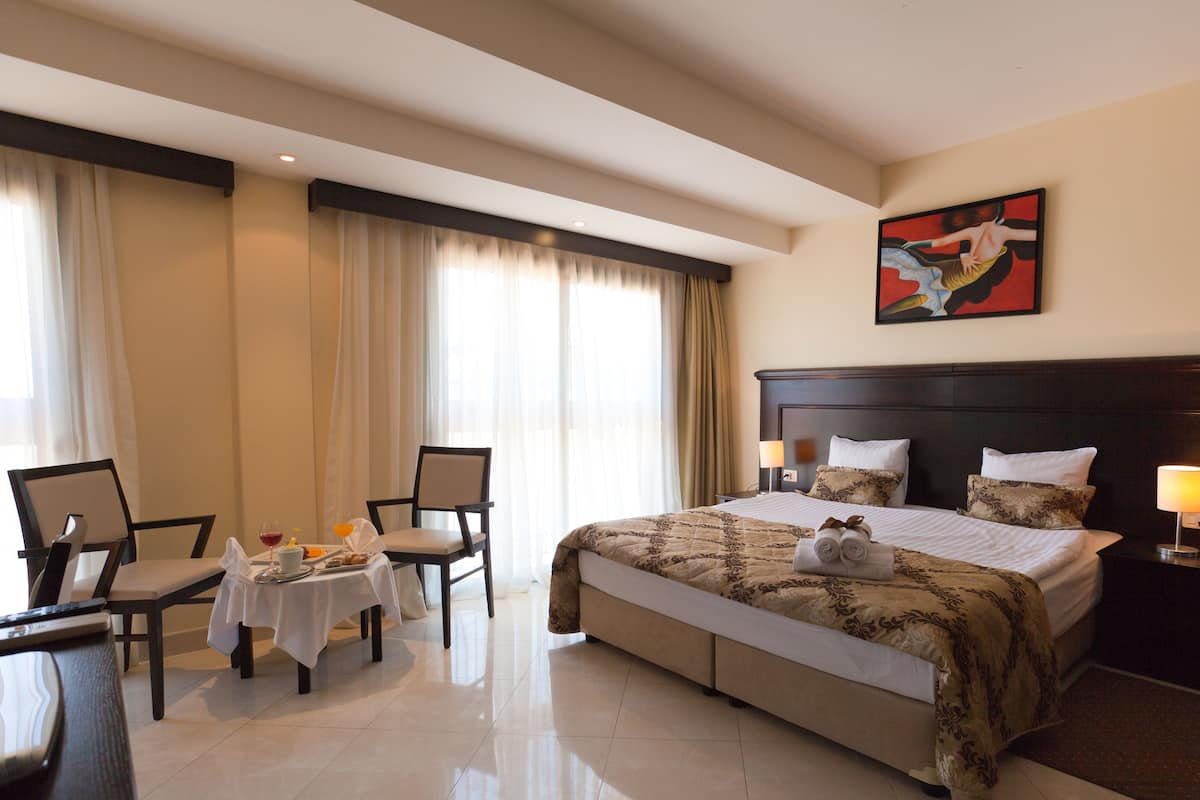 Habitación de hotel con una cama grande, un escritorio con una silla, una mesa con alimentos para el desayuno y un cuadro en la pared.