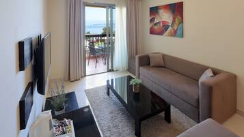 Una sala de estar moderna con sofá, una mesa de centro, televisor y un balcón con vistas al mar.