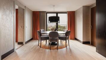 A modern dining area with a round table and six chairs, a large window with curtains, and a view of the city.