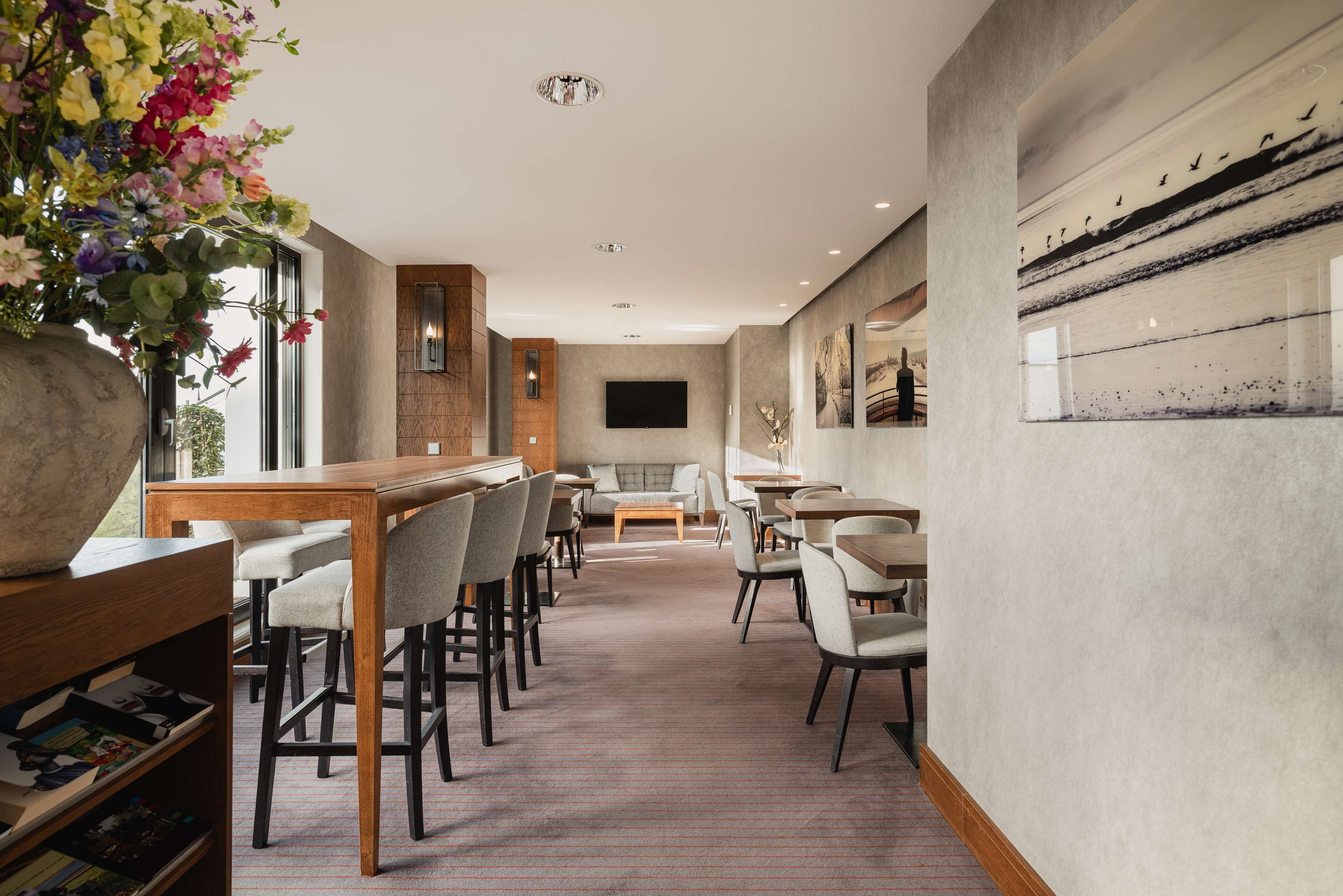 Eine moderne Hotelhalle mit einer langen Rezeption, mehreren Sitzbereichen und einem großen Fenster mit Blick ins Freie.