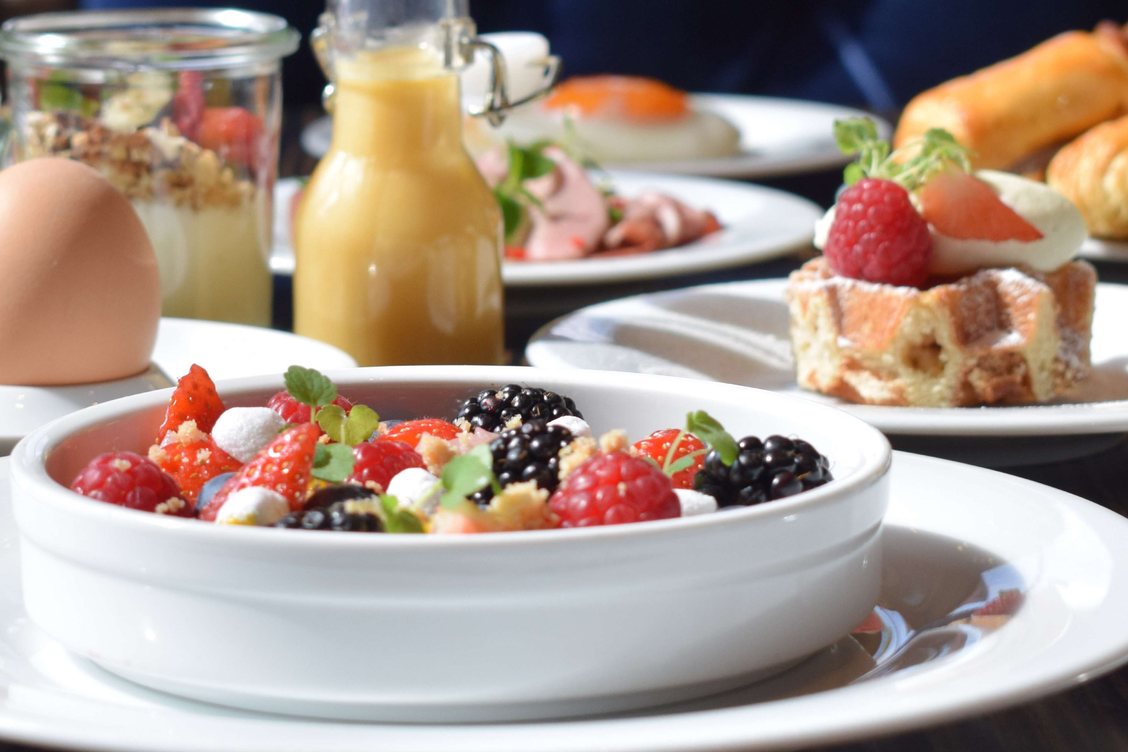 A breakfast setting with a bowl of mixed berries and cream, a bottle of juice, and pastries on a table.