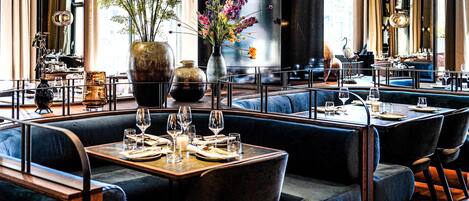 Un restaurante con cabinas, mesas y un jarrón grande con flores.