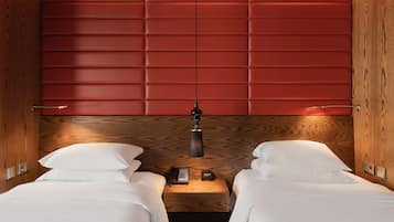 Habitación de hotel con dos camas, cabecero de madera, mesita de noche con lámpara y un reloj.