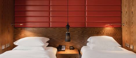 Habitación de hotel con dos camas, cabecero de madera, mesita de noche con lámpara y un reloj.