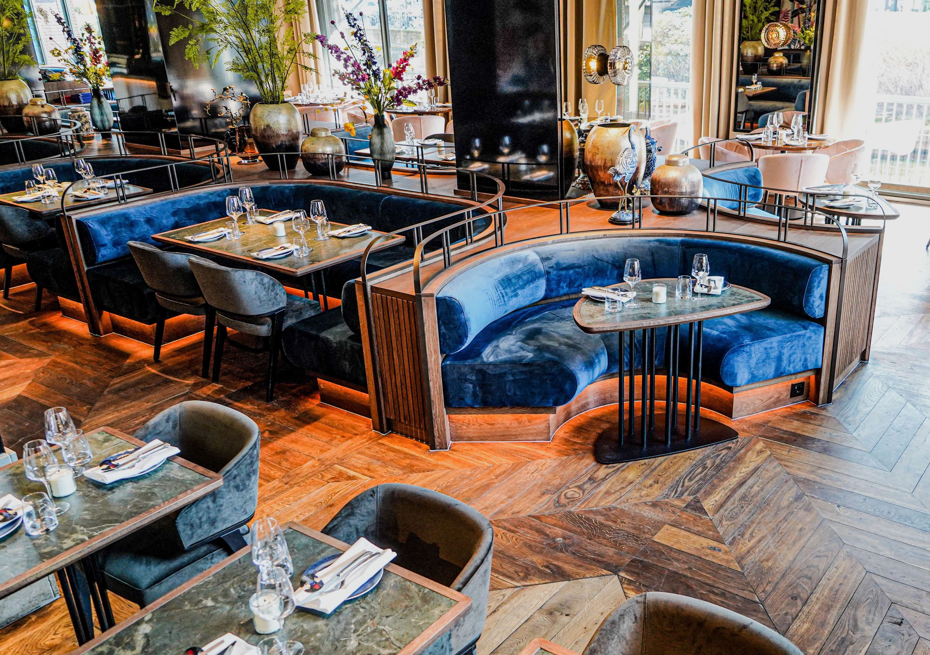 A restaurant with round tables, blue velvet sofas, and a herringbone wooden floor.