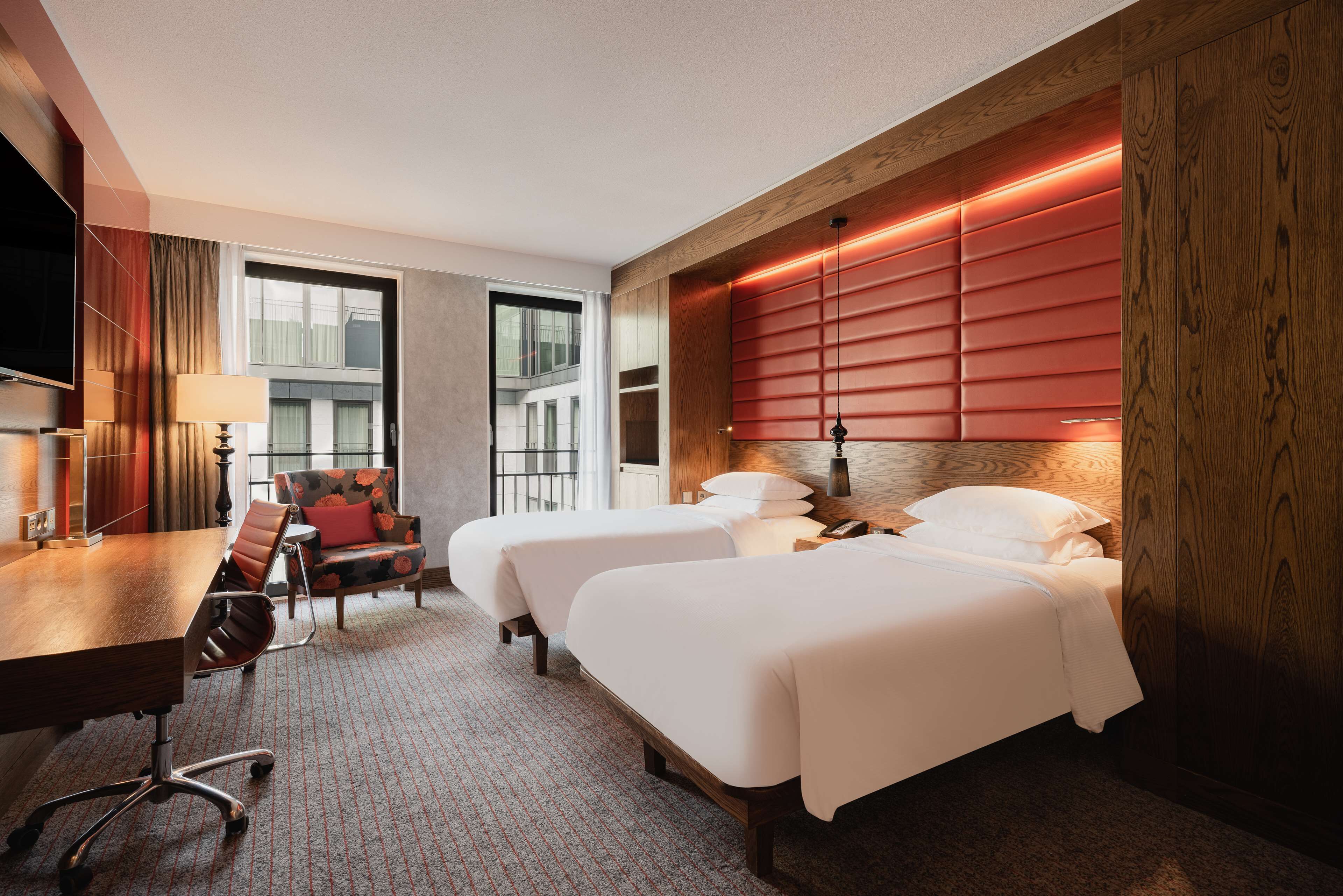 Ein Hotelzimmer mit zwei Betten, einem Schreibtisch mit Stuhl, einem Fernseher und einem großen Fenster.